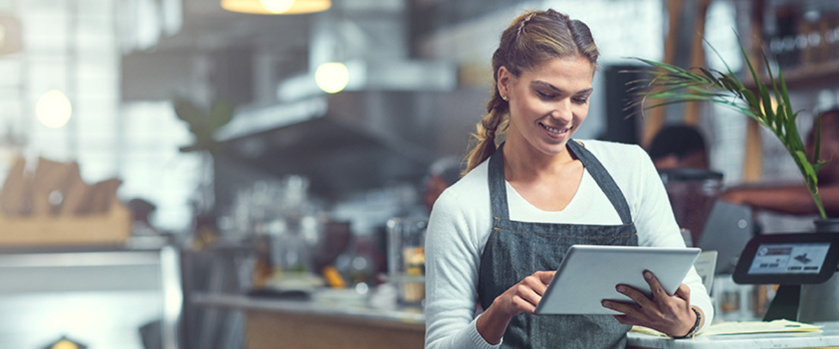 Small business owner using a tablet to review financial metrics and manage overhead expenses due to inflation.