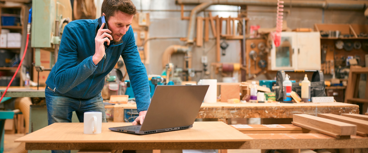 A male small business owner in manufacturing on his phone learning how to manage cash flow fluctuations with short-term business loans