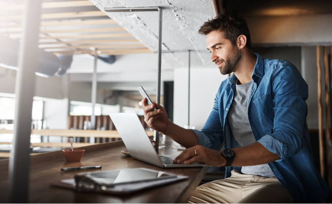 Man Working On His Phone And Computer To Run His Business
