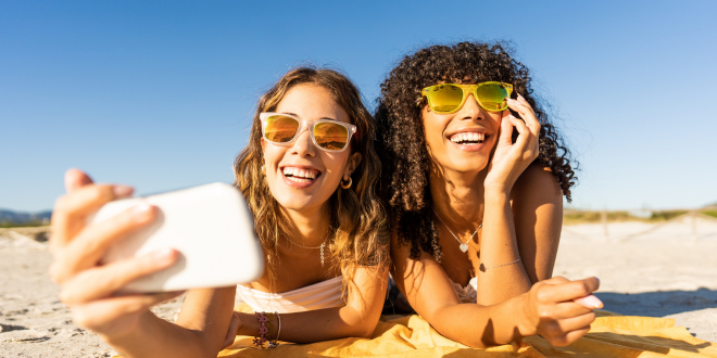 Image Of Two Friends On Their Phone At The Beach Sharing Their Banking Experience
