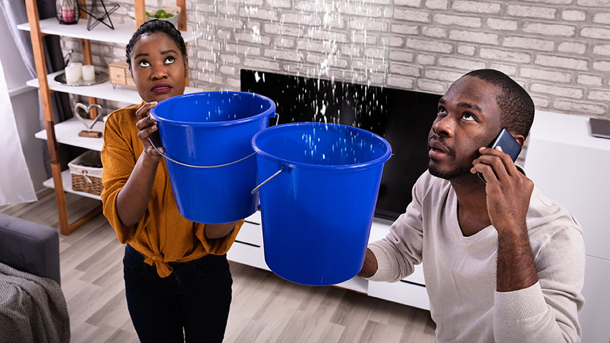 image of couple holding buckets to catch water from ceiling