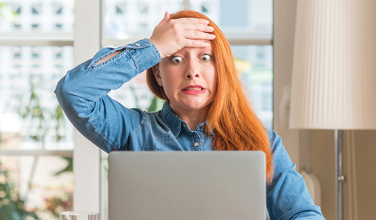 Image of woman looking at computer with hand on forehead
